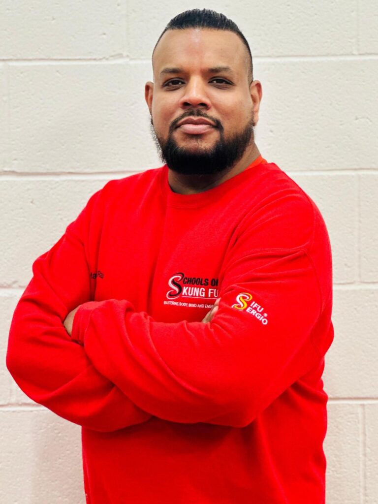 Profile picture of SiFu Kul wearing a red sweatshirt with the SOKF master logo, arms folded and smiling, exuding a confident and approachable presence.